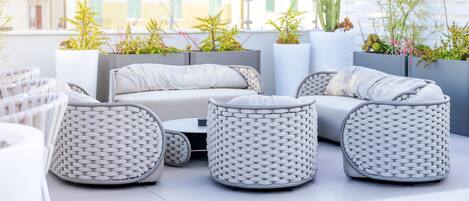 A modern outdoor seating area with wicker furniture, a white sofa, and potted plants.