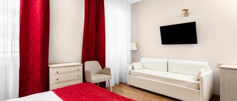 A hotel room with a bed, a white sofa, a small table, a chair, and a TV mounted on the wall.