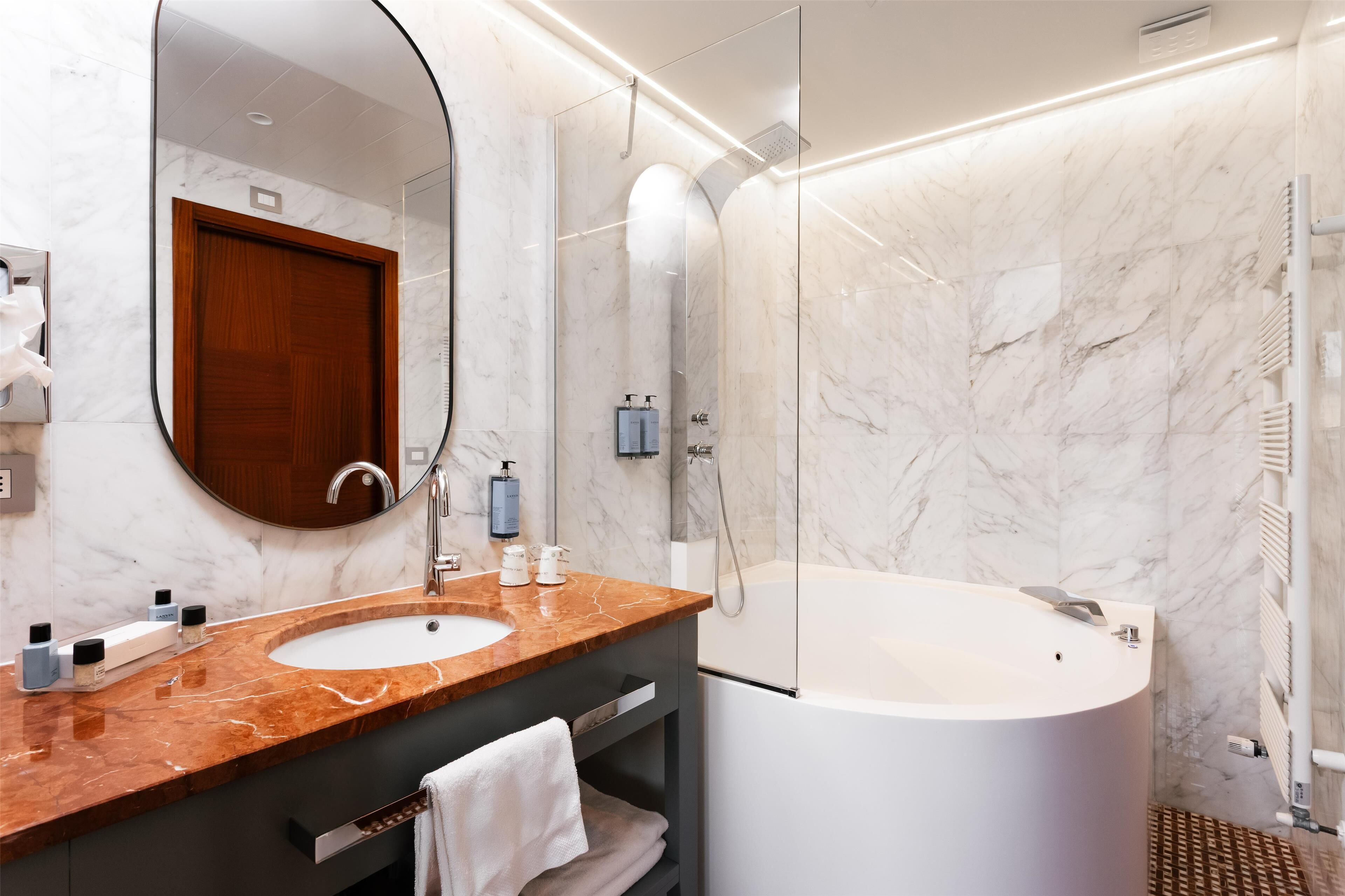 Un baño moderno con tocador de mármol, un espejo grande, una bañera y un box de ducha.