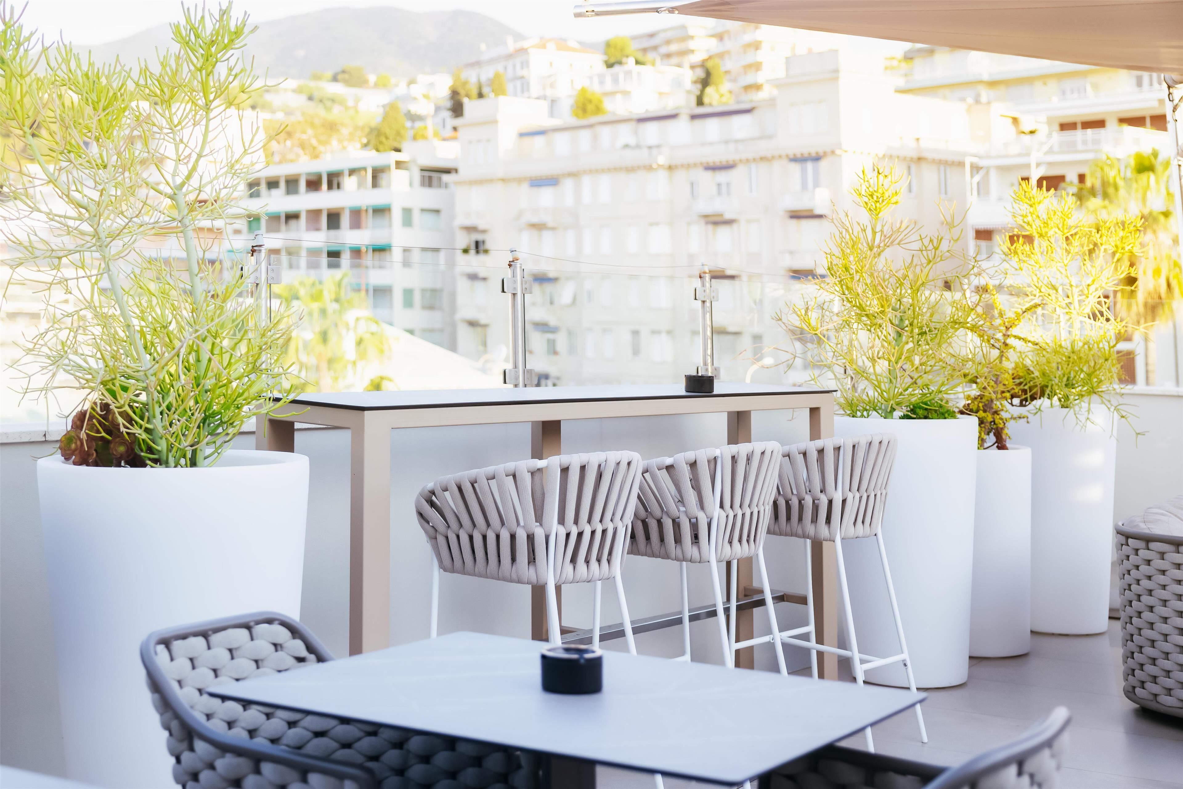 A rooftop terrace with a table and chairs, potted plants, and a view of residential buildings.