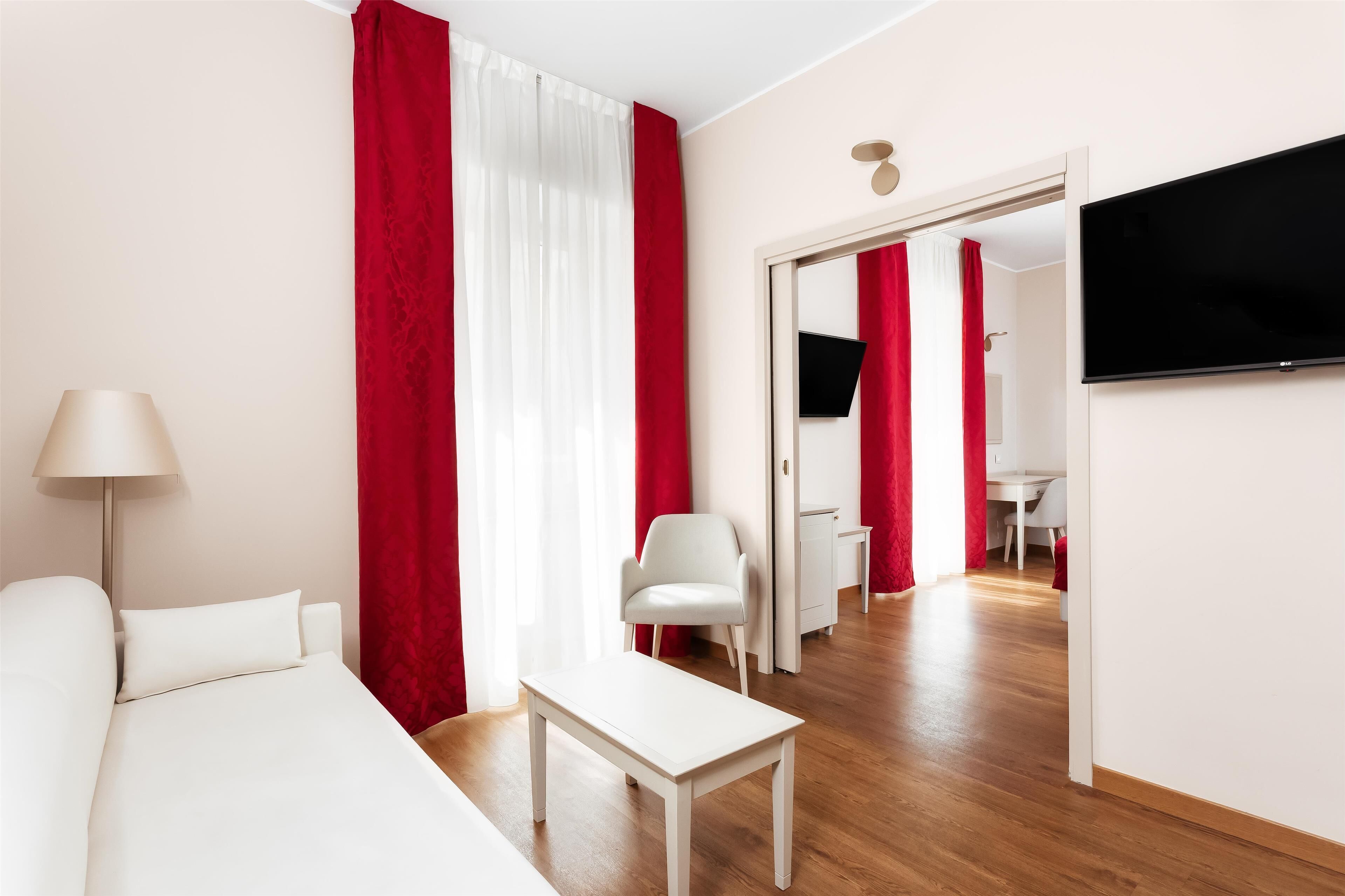 Ett hotellrum med en säng, ett vitt bord, en stol, en tv och en matplats med ett bord och stolar.
