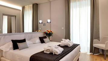 Un lit bien fait, avec des draps blancs, une couverture sombre et deux serviettes posées sur le lit. On aperçoit un vase rempli de fleurs sur la table de chevet, à côté du lit.
