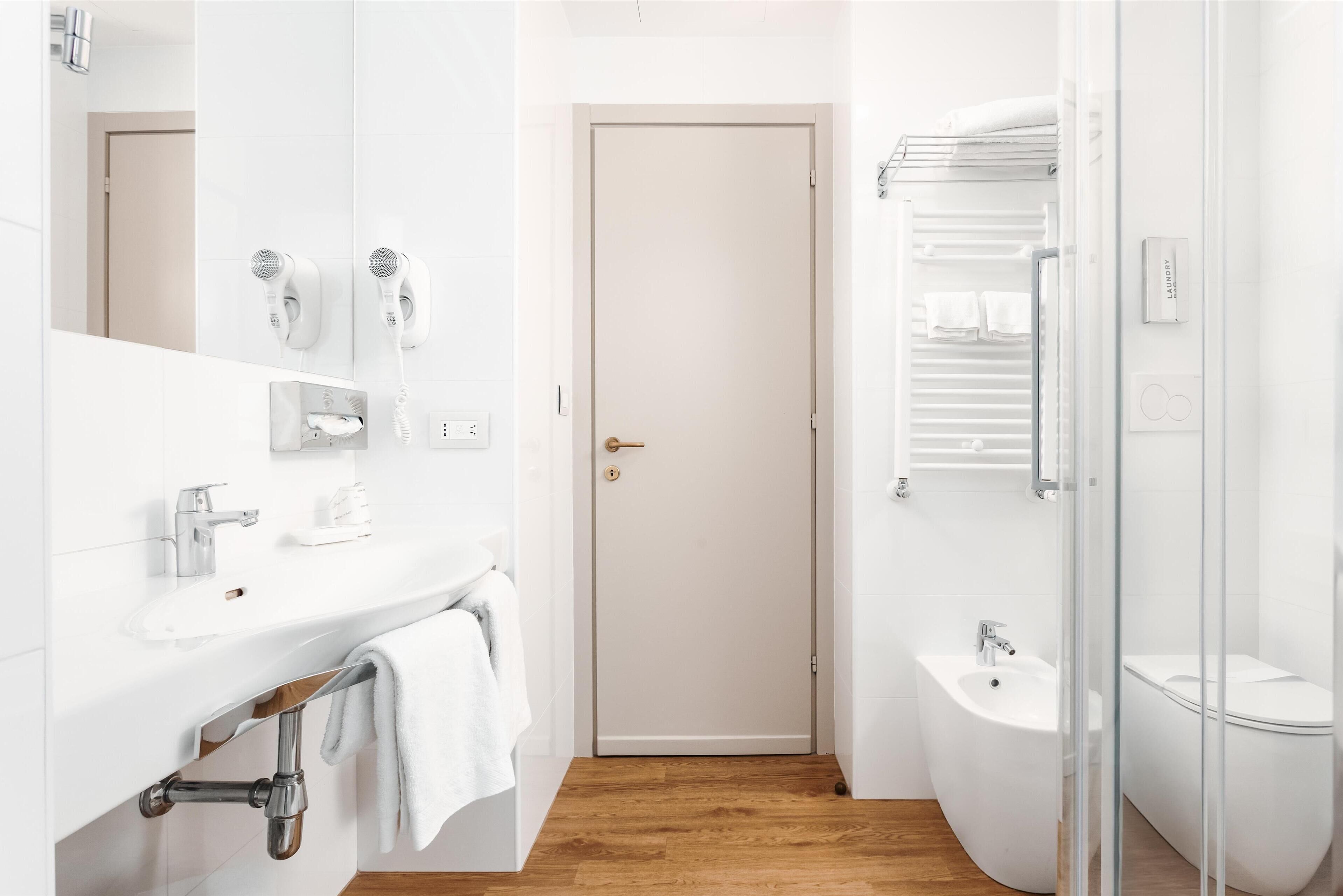 A modern bathroom with a white sink, a mirror, a towel rack, a shower area, and a toilet.