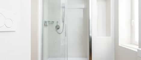 A modern shower with a glass door, a wooden floor, and white tiled walls.