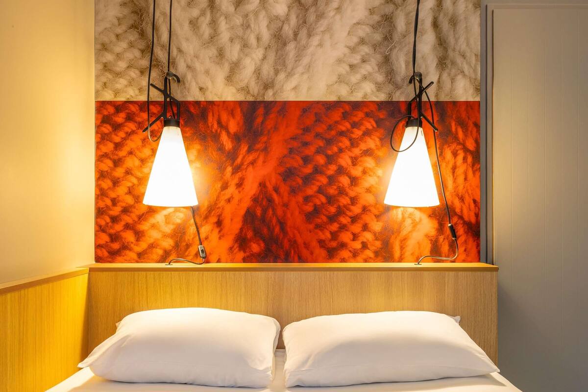 Quarto de hotel com uma cama, duas luminárias pendentes e uma parede texturizada acima da cama.