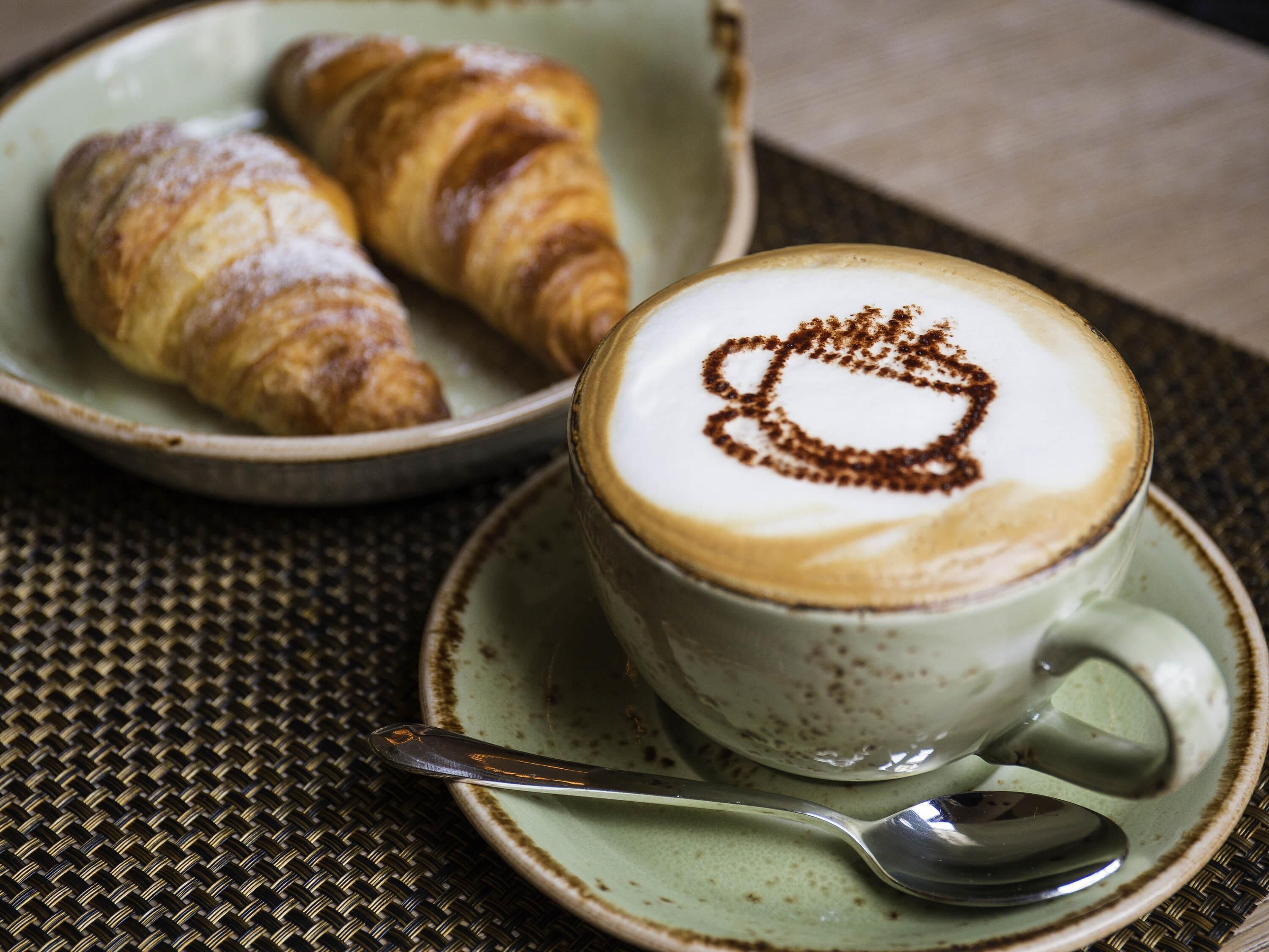 Une tasse de café agrémentée d’un motif en latte art et une assiette de croissants.