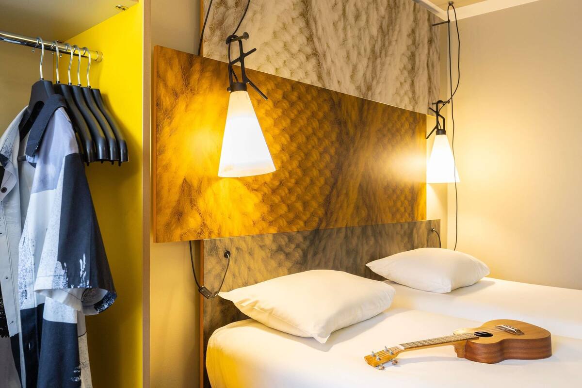 Quarto de hotel com uma cama, um violão e um cabideiro.