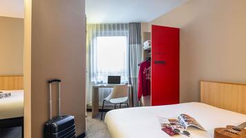 Une chambre d’hôtel avec un lit, un bureau avec un ordinateur portable, une valise et une armoire rouge.