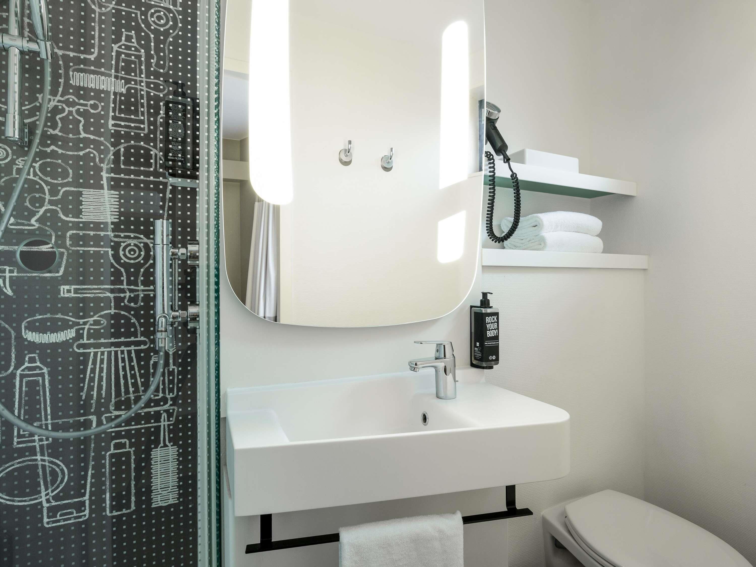A modern bathroom with a glass shower enclosure, a white sink, a mirror, and a toilet.