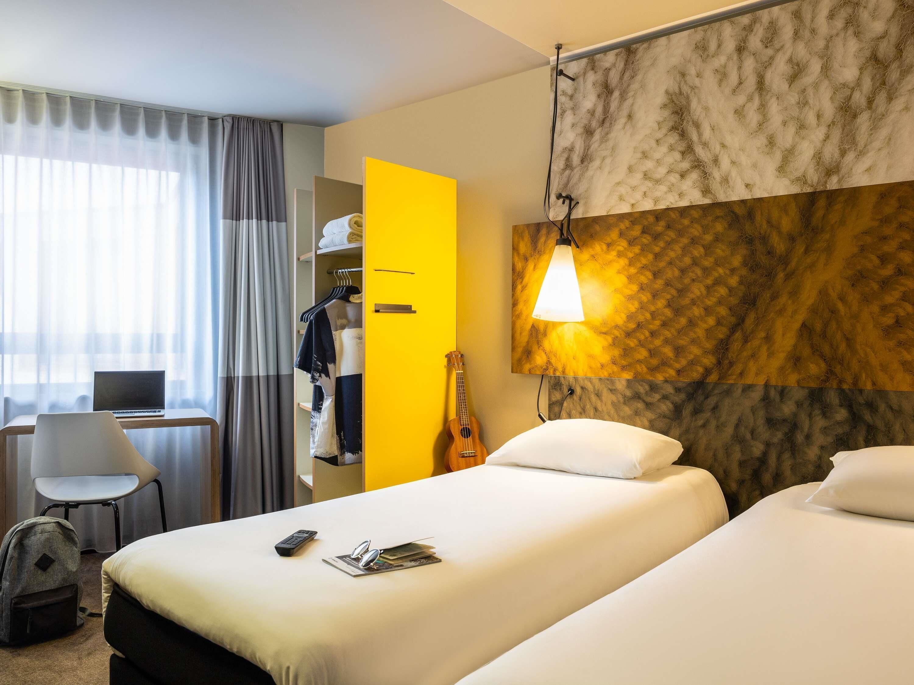 A hotel room with a bed, a desk with a laptop, a chair, a guitar, and a wardrobe.