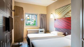 Een hotelkamer met twee bedden, een televisie, een raam met uitzicht op gebouwen en een lamp.