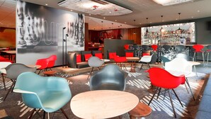 Un café moderno con una zona de bar, asientos con sillas rojas y grises, y un gran mural en la pared.