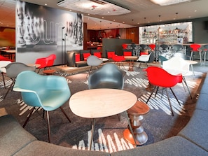 Un café moderne doté d’un bar, de tables et de chaises rouges et grises, et d’une grande fresque murale.