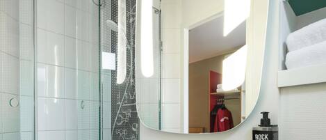 Un baño moderno con un lavamanos blanco, un espejo grande y una ducha con puerta de cristal.