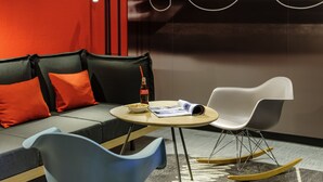 Una habitación moderna con un sofá gris, cojines anaranjados, una pequeña mesa redonda, una silla blanca y un sillón mecedora.