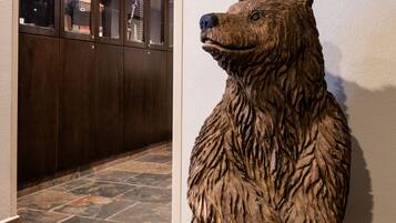 Un suelo de baldosas de piedra, un mueble de madera con puertas de cristal, y una escultura de madera de un oso con un letrero que dice 'Gift Shop'.