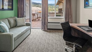 A hotel room with a sofa, a desk with a laptop, a chair, and a balcony with a view of the mountains. - Yosemite Southgate Hotel & Suites (Oakhurst)