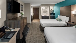 A hotel room with two beds, a desk with a laptop, a TV mounted on the wall, and a bathroom with a sink and mirror. - Yosemite Southgate Hotel & Suites (Oakhurst)