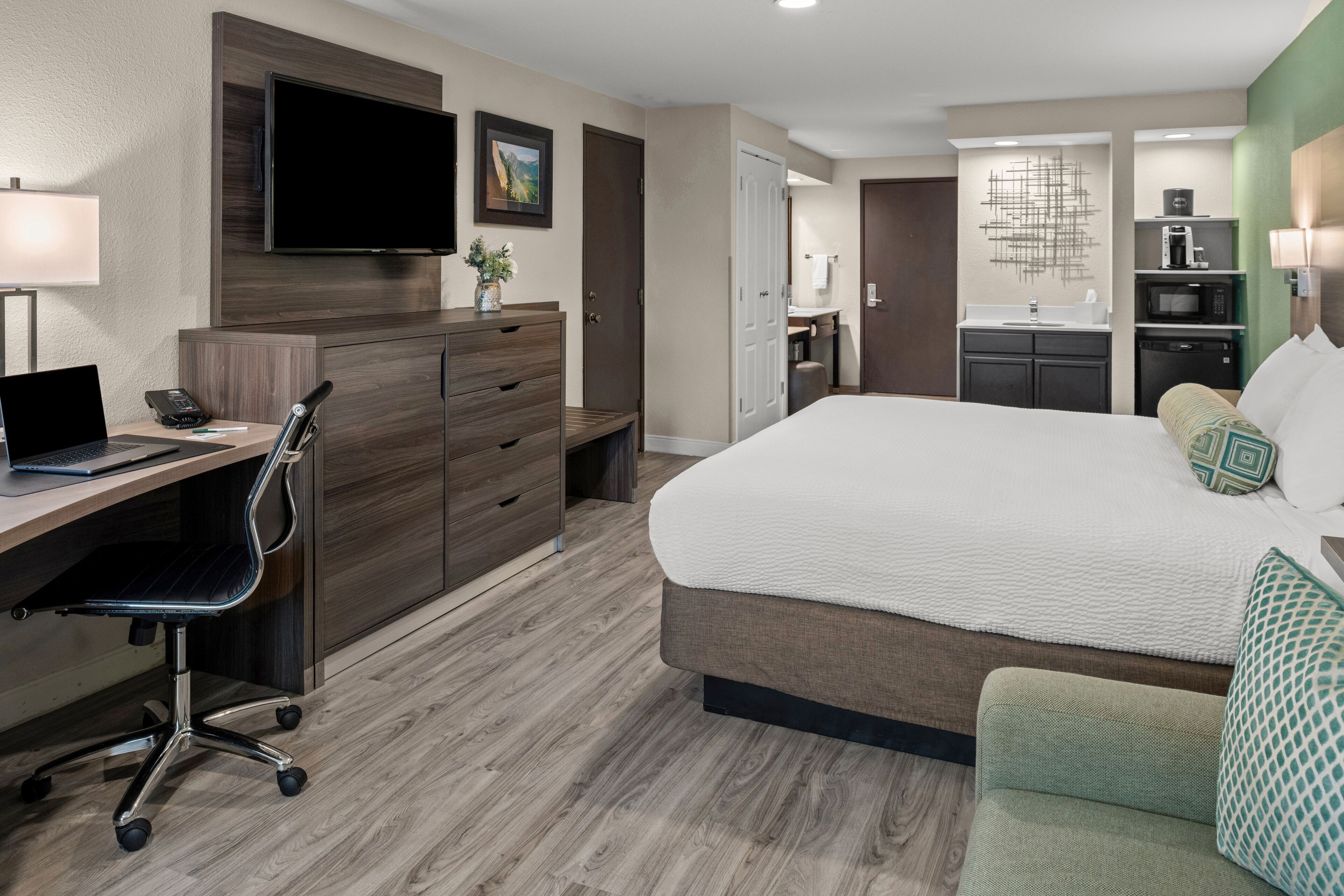 A hotel room with a bed, desk, chair, and a kitchenette.