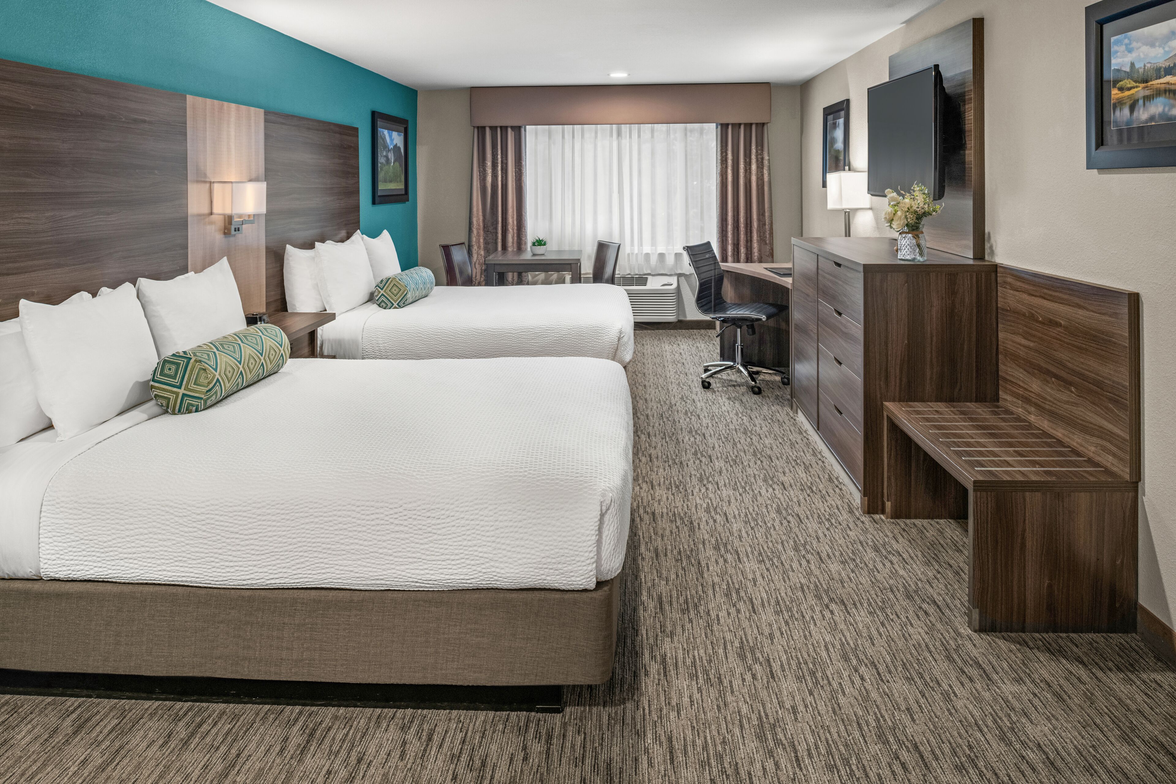 A hotel room with two beds, a desk, a chair, a dresser, and a TV.