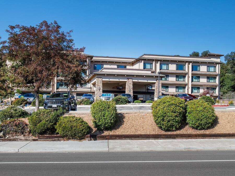 A hotel with a stone facade, multiple balconies, and a parking lot with several vehicles.