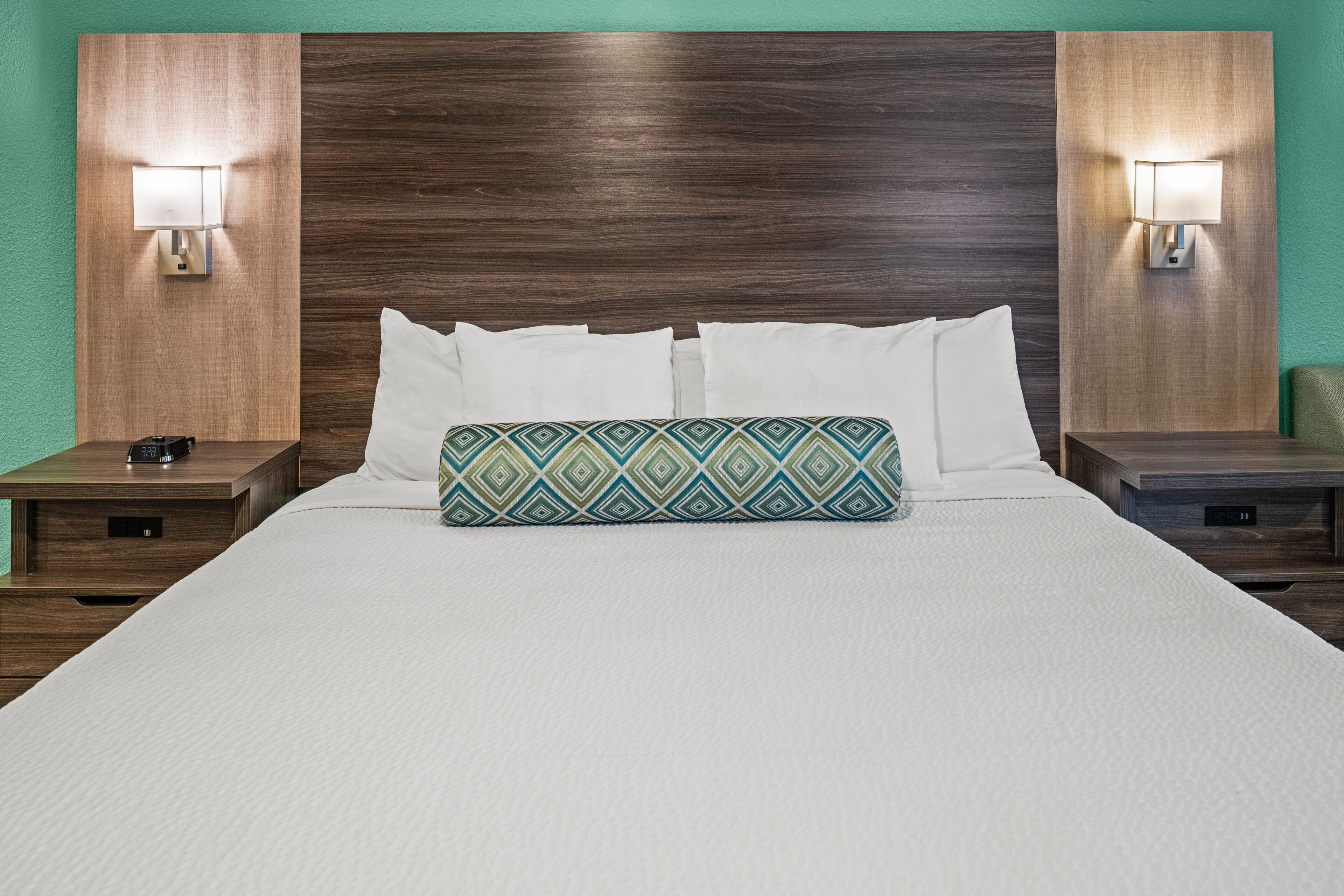 A neatly made bed with white linens, a decorative pillow, and two bedside tables with lamps.