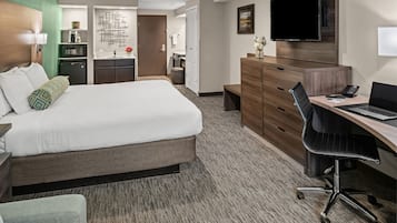 Habitación de hotel con una cama grande, un escritorio con una computadora portátil, un televisor, un microondas y una kitchenette pequeña.