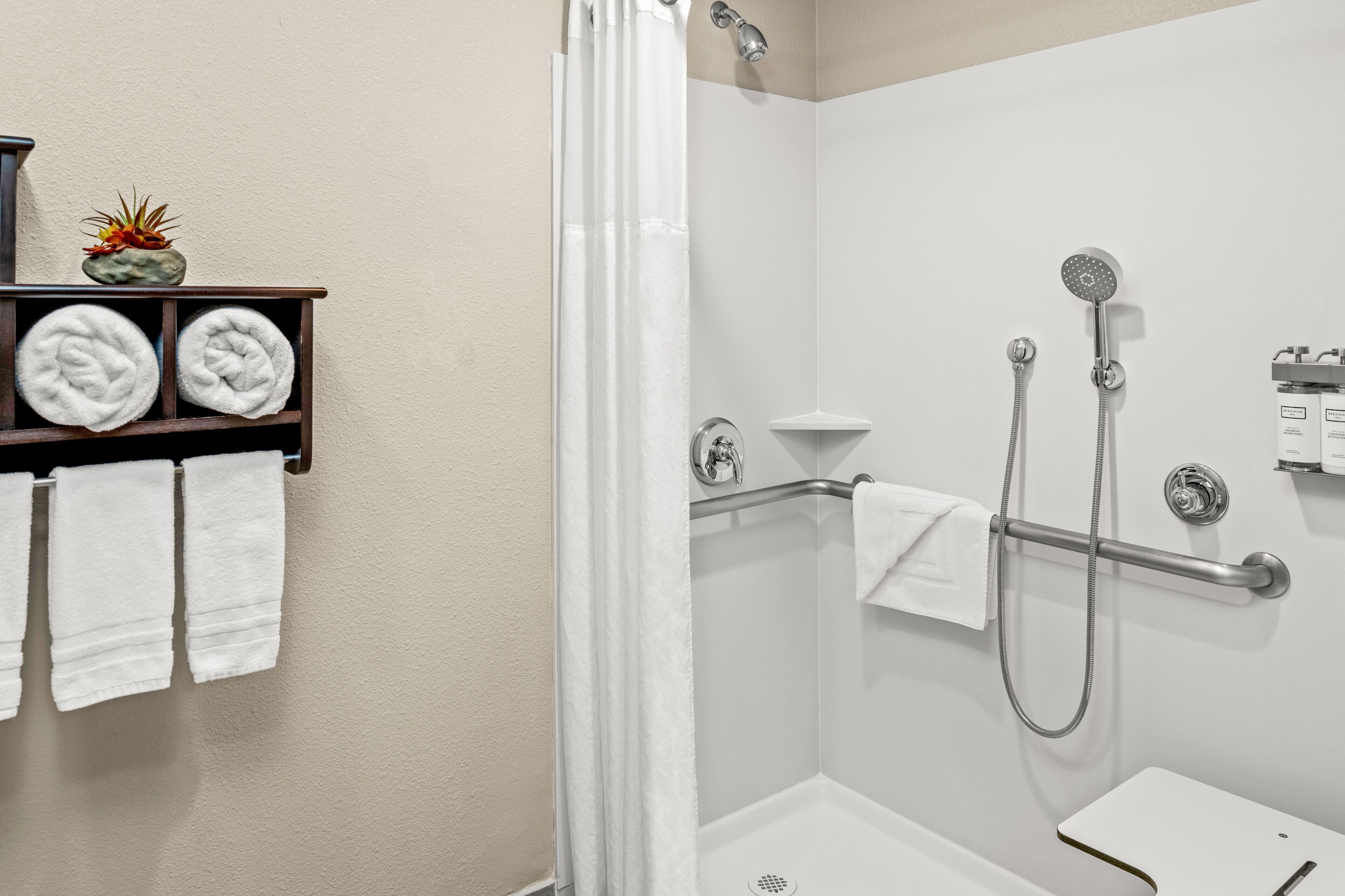 Un baño moderno con ducha envuelta en vidrio, lavamanos blanco y un perchero con toallas dobladas ordenadamente.