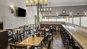 A restaurant with wooden tables and chairs, a long counter, and pendant lighting. - Yosemite Southgate Hotel & Suites (Oakhurst)