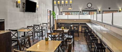 Un restaurante con mesas y sillas de madera, una barra alargada e iluminación colgante.