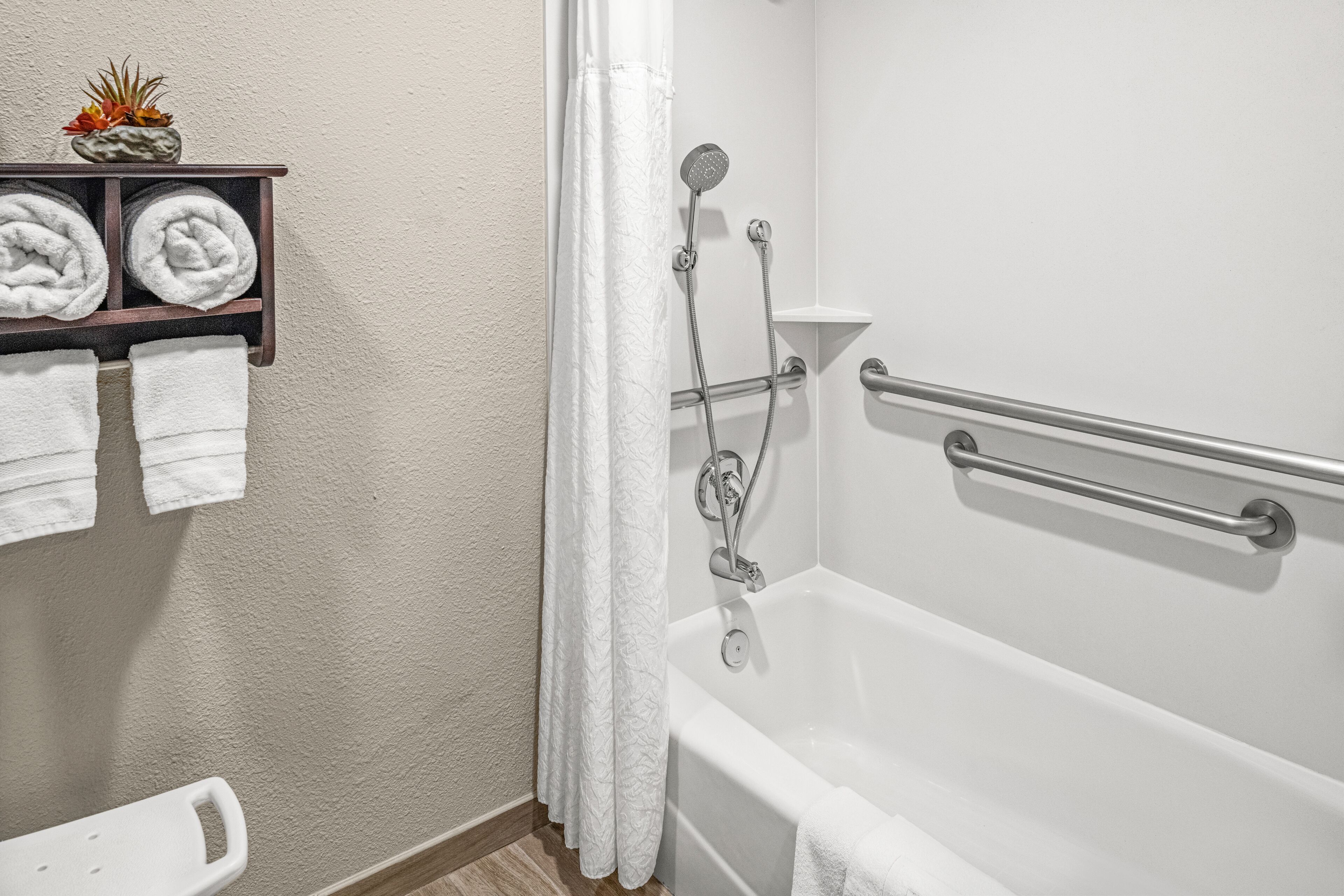 Un baño con bañera, ducha con cabezal de ducha de mano, toallero con toallas y un estante pequeño con una planta.