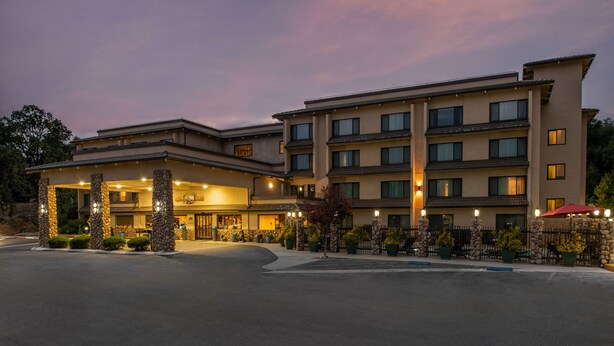 A multi-story hotel with a covered entrance, stone pillars, and a landscaped driveway. - Yosemite Southgate Hotel & Suites (Oakhurst)