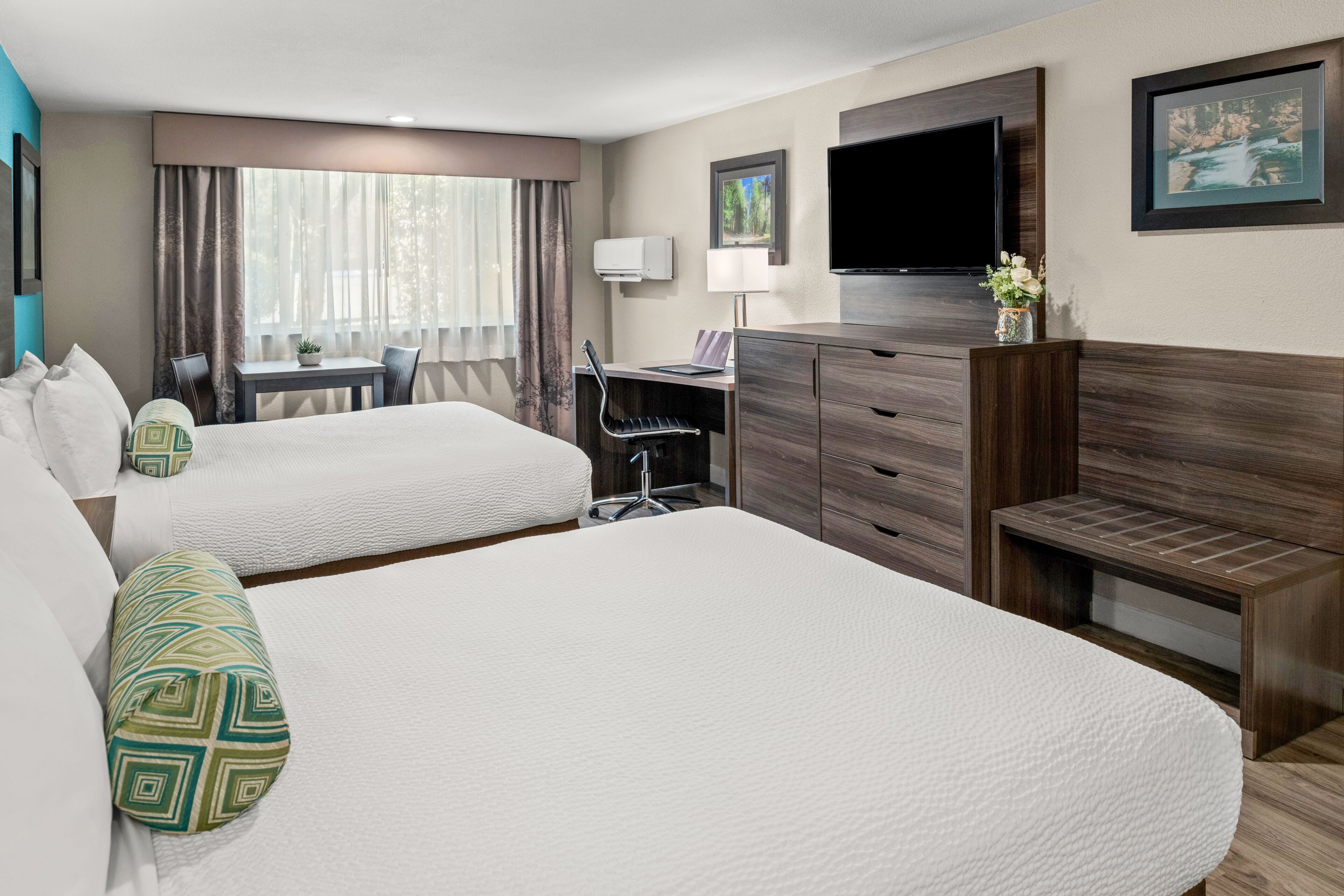Une chambre d’hôtel avec deux lits, un bureau, une chaise, une télévision et une fenêtre avec des rideaux.