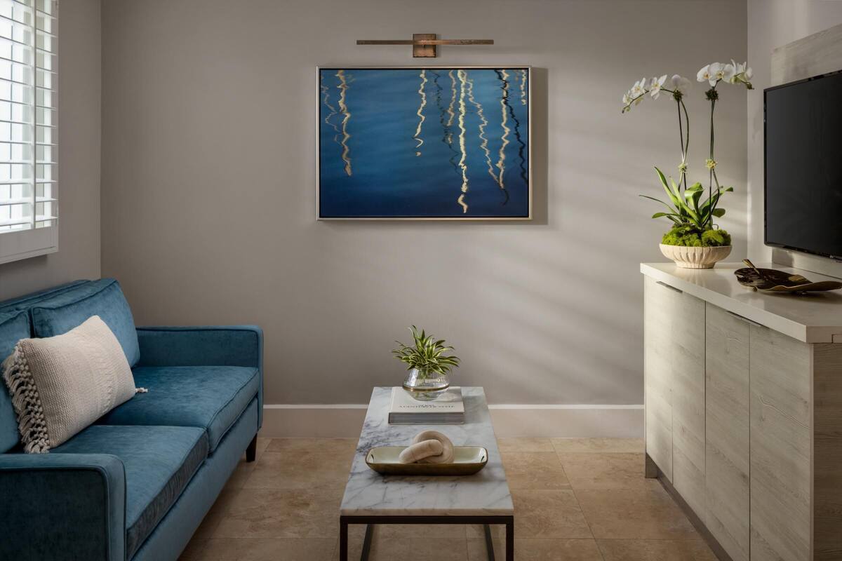 A modern living room with a blue sofa, a marble coffee table, a painting, and a TV on a wooden cabinet.