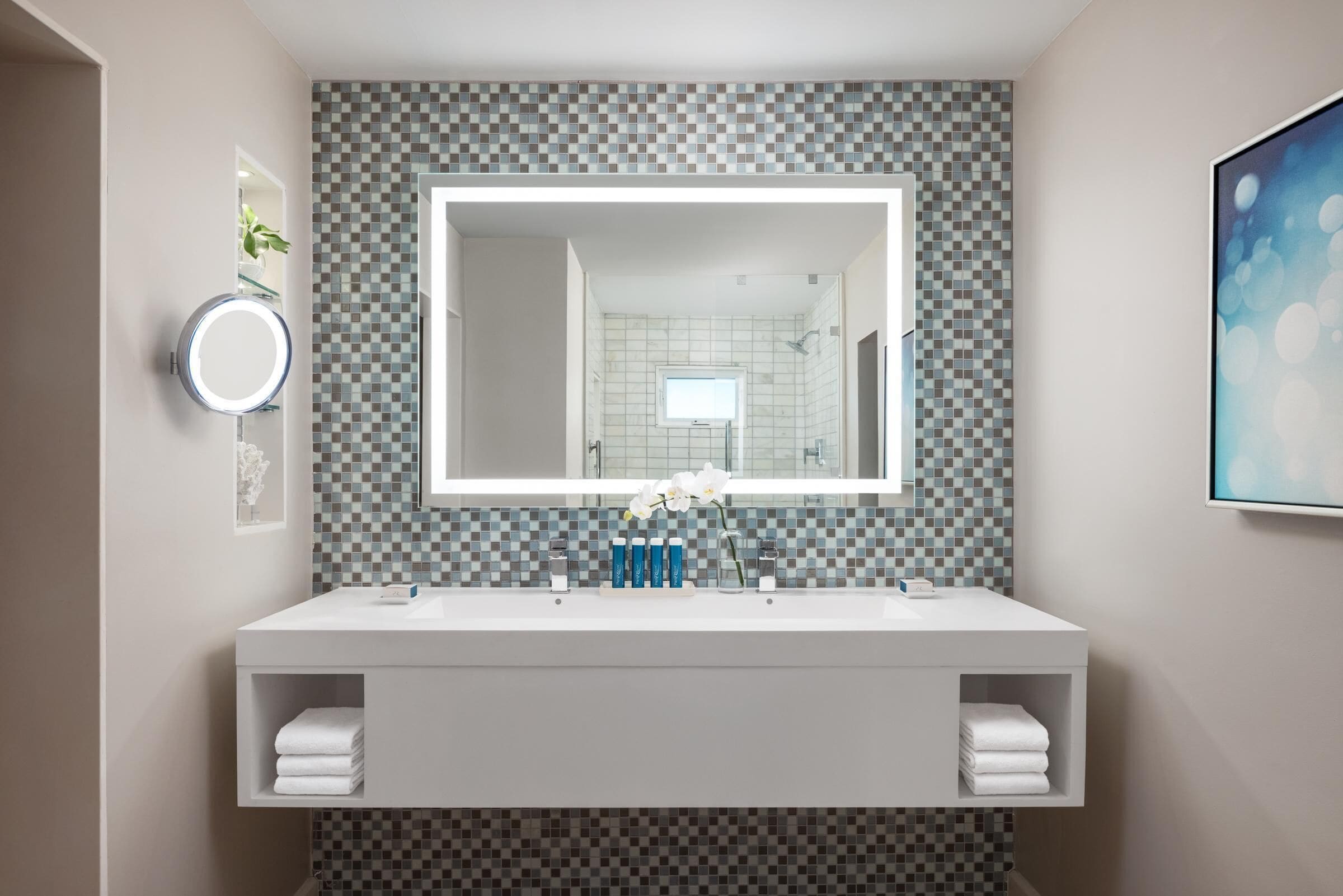 Een moderne badkamer met een grote spiegel, twee wasbakken en een betegelde spatwand.