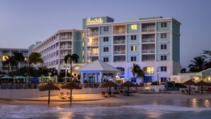 Ett hotell vid stranden med flera balkonger, ett poolområde och sittplatser precis vid stranden.