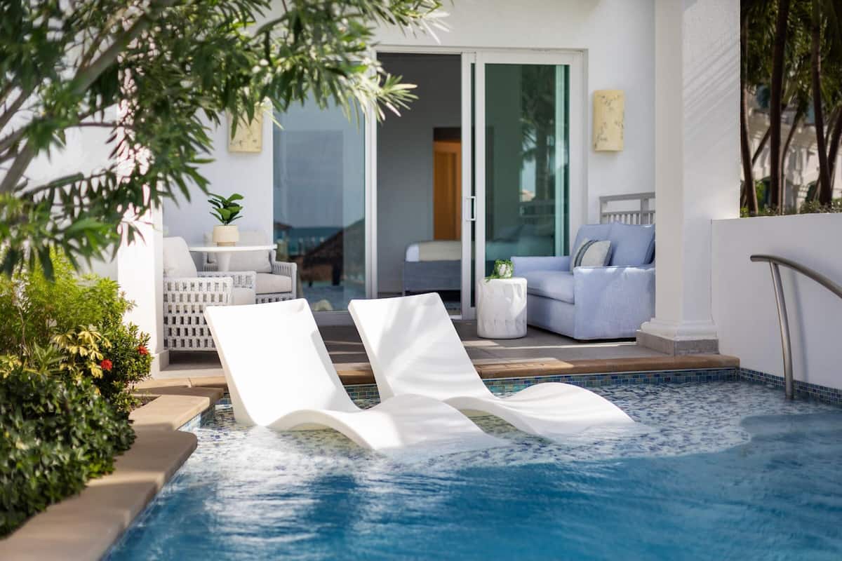 A pool area with lounge chairs, a sofa, and a sliding glass door leading to a bedroom.