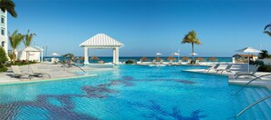 A pool area with lounge chairs, umbrellas, and a pavilion overlooking the sea.