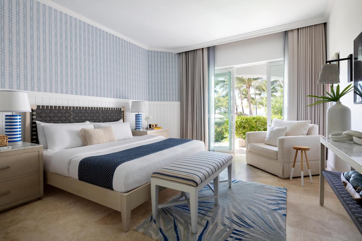 A modern hotel room with a large bed, a desk, a sofa, and a view of palm trees.
