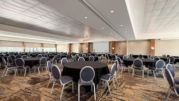 A large conference room with multiple round tables and chairs, a projector screen, and an American flag.