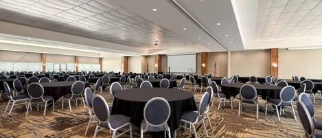 A large conference room with multiple round tables and chairs, a projector screen, and an American flag.