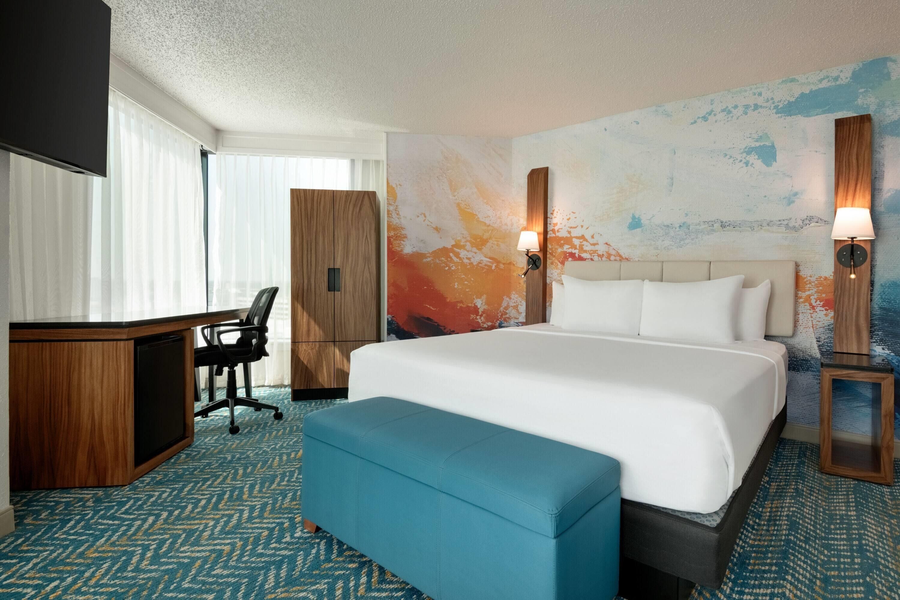 A hotel room with a large bed, a desk, a chair, and a TV.