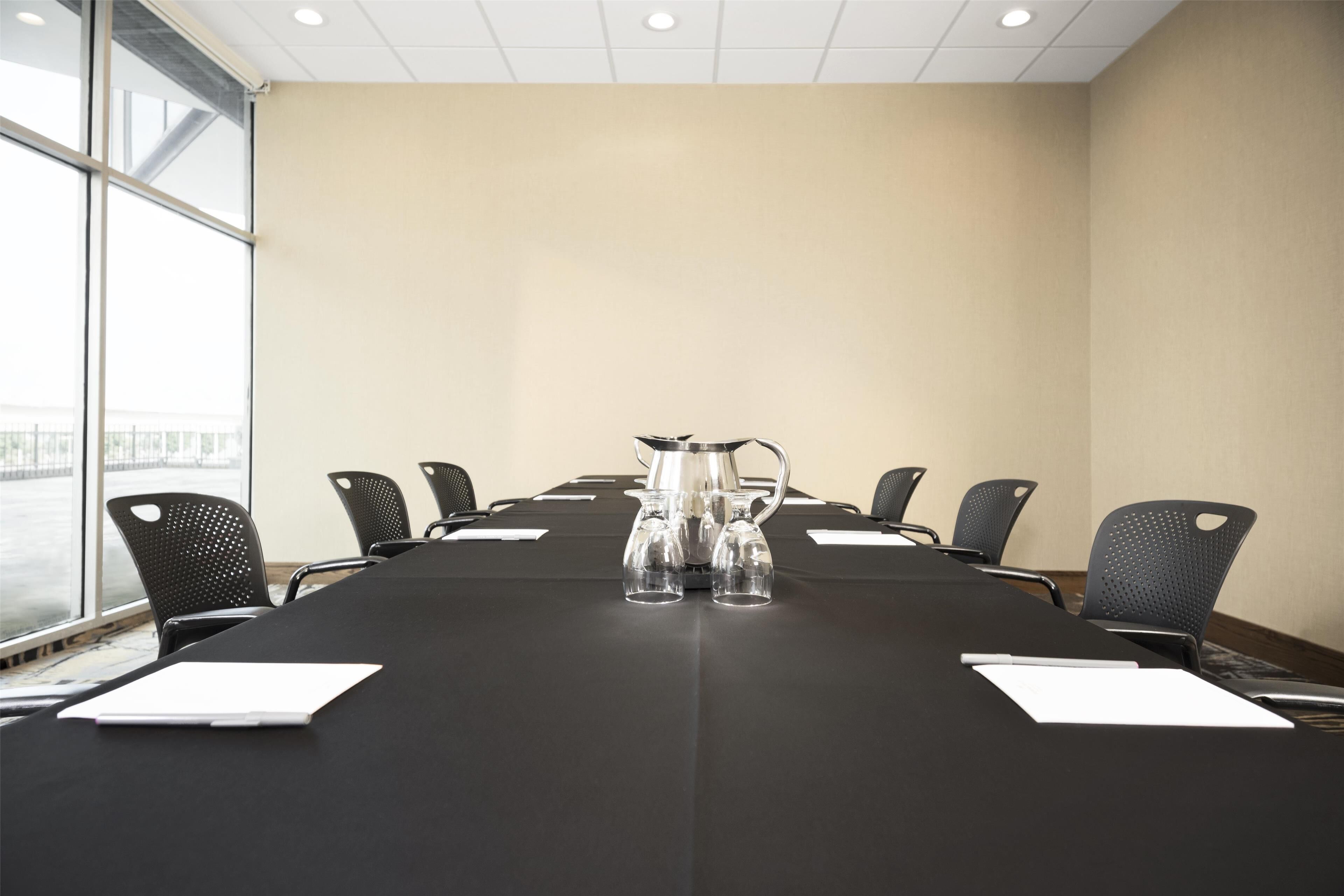 Une salle de conférence avec une longue table, des chaises noires et une carafe d’eau.