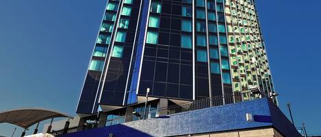 A tall hotel with a modern design, featuring a prominent entrance and outdoor seating area.