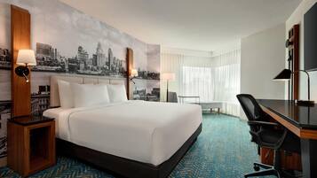 A hotel room with a large bed, a desk, a chair, and a cityscape mural on the wall.