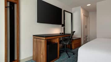 Une chambre d’hôtel avec un bureau en bois, une chaise noire, un lit, un grand miroir et un téléviseur à écran plat.