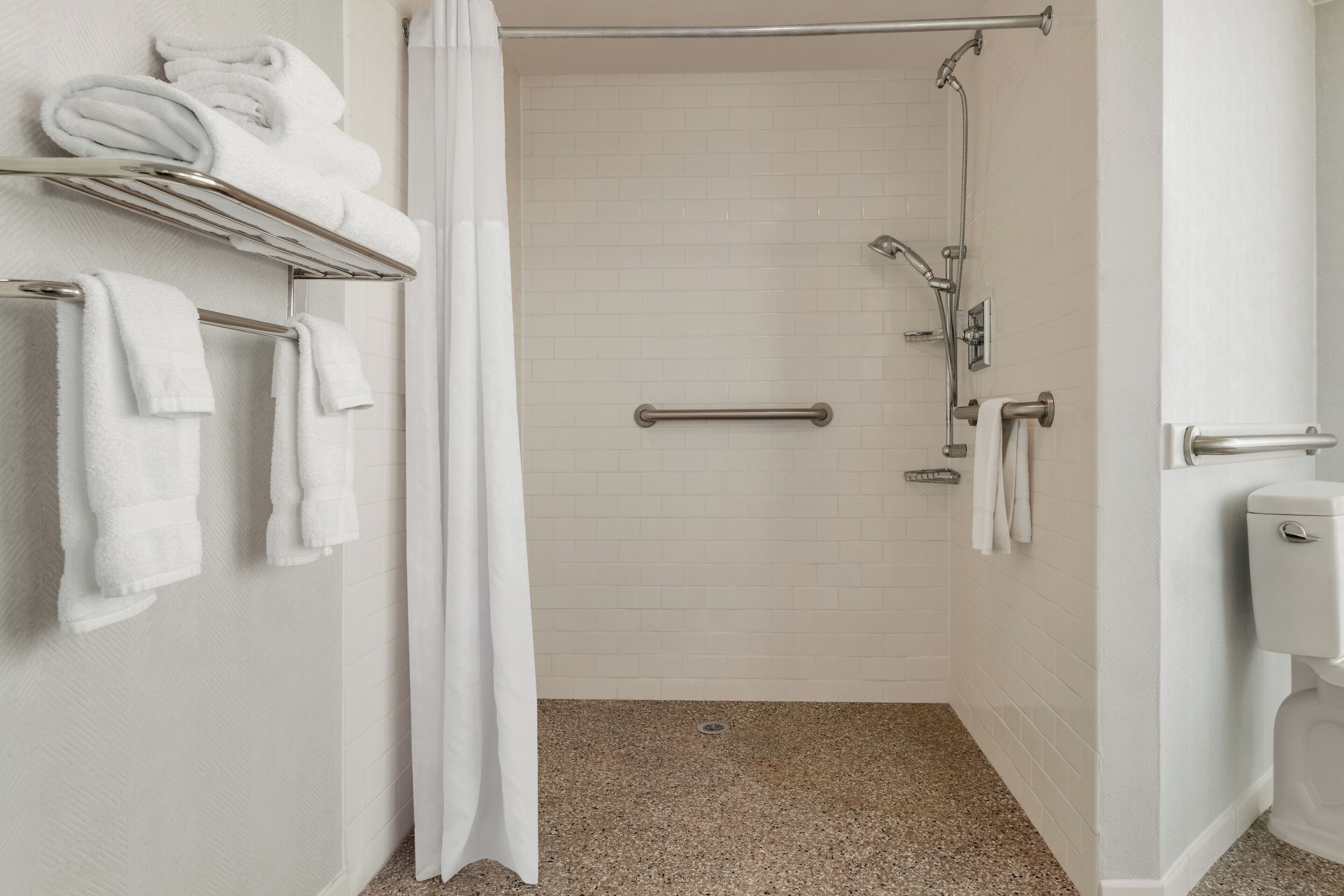 Une salle de bain équipée d’une douche, de toilettes et d’un porte-serviettes avec des serviettes pliées.