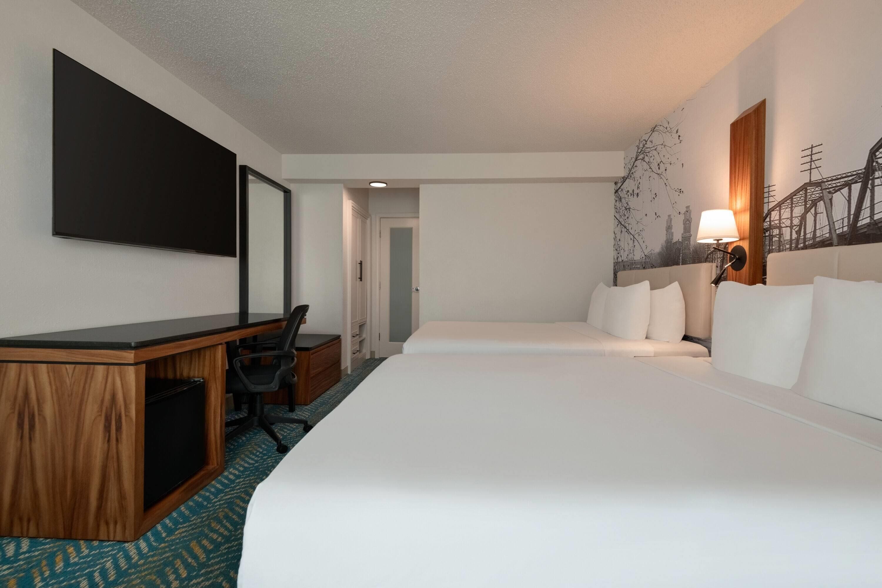 Habitación de hotel con una cama grande, un escritorio con computadora, una silla y un televisor instalado en la pared.