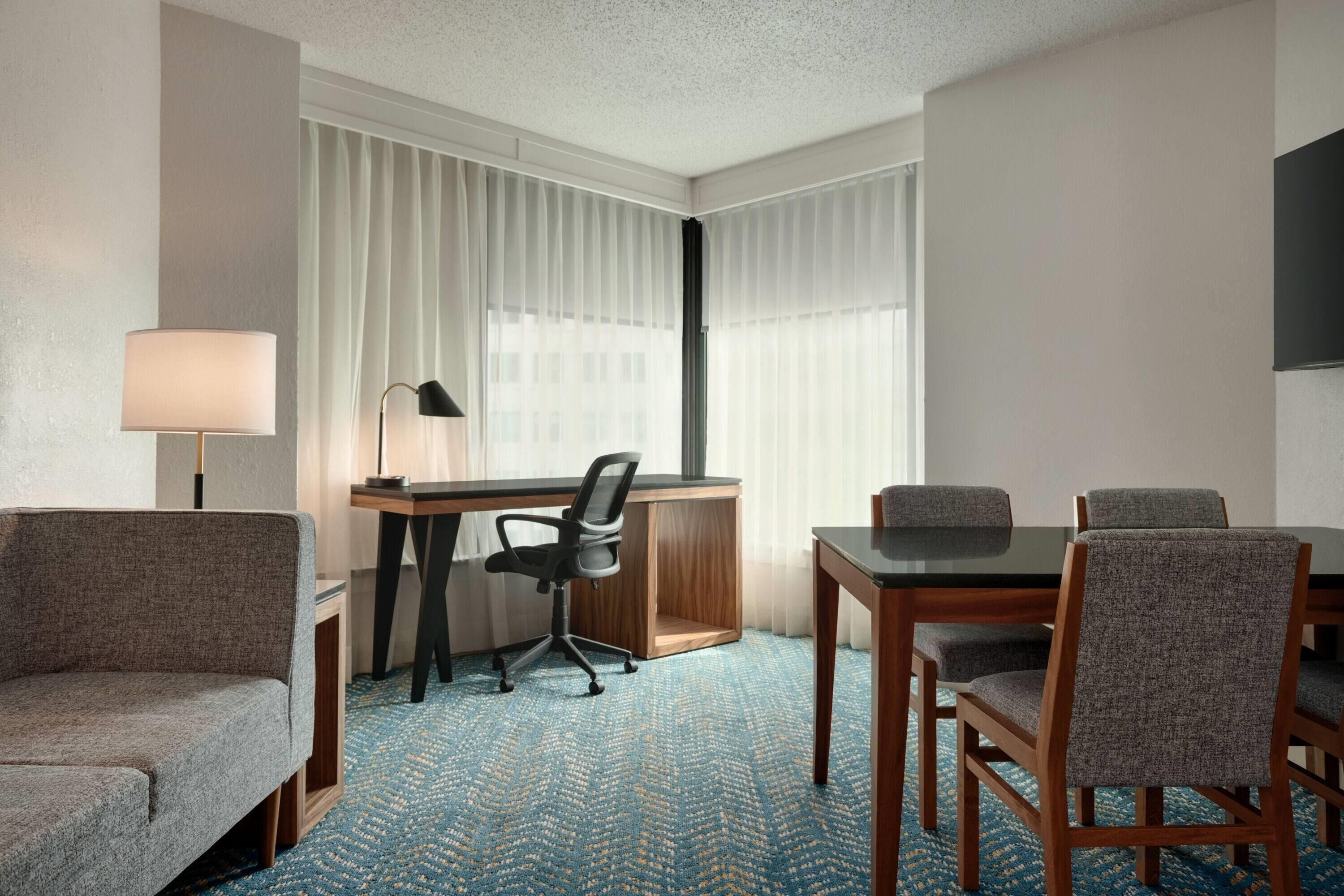 Ein Hotelzimmer mit Schreibtisch, zwei Stühlen, einer Couch und einer Lampe.