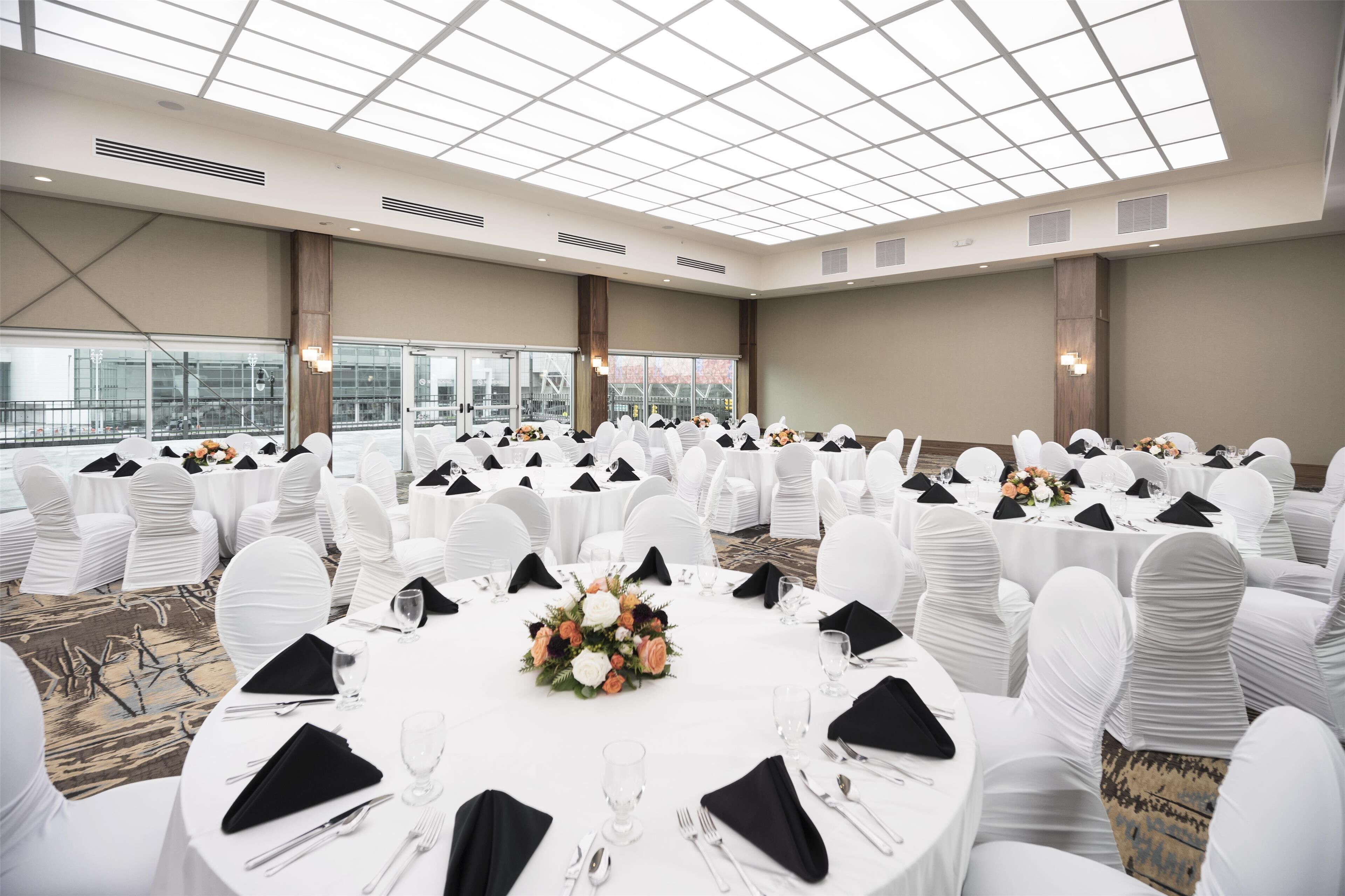 A banquet hall with round tables, white chairs, and a high ceiling with skylights.